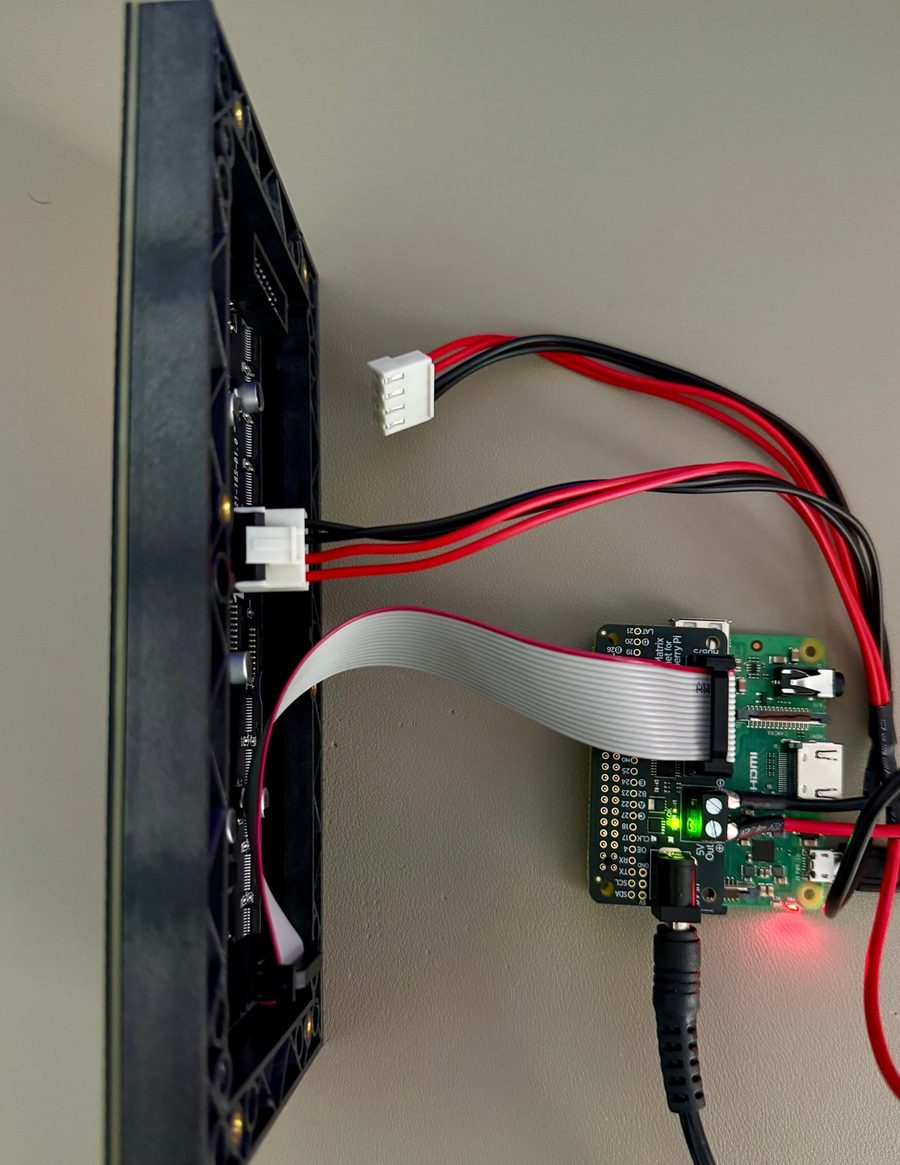 The back of the LED panel, wired by ribbon cable and power leads to a Raspberry Pi with a matrix bonnet
